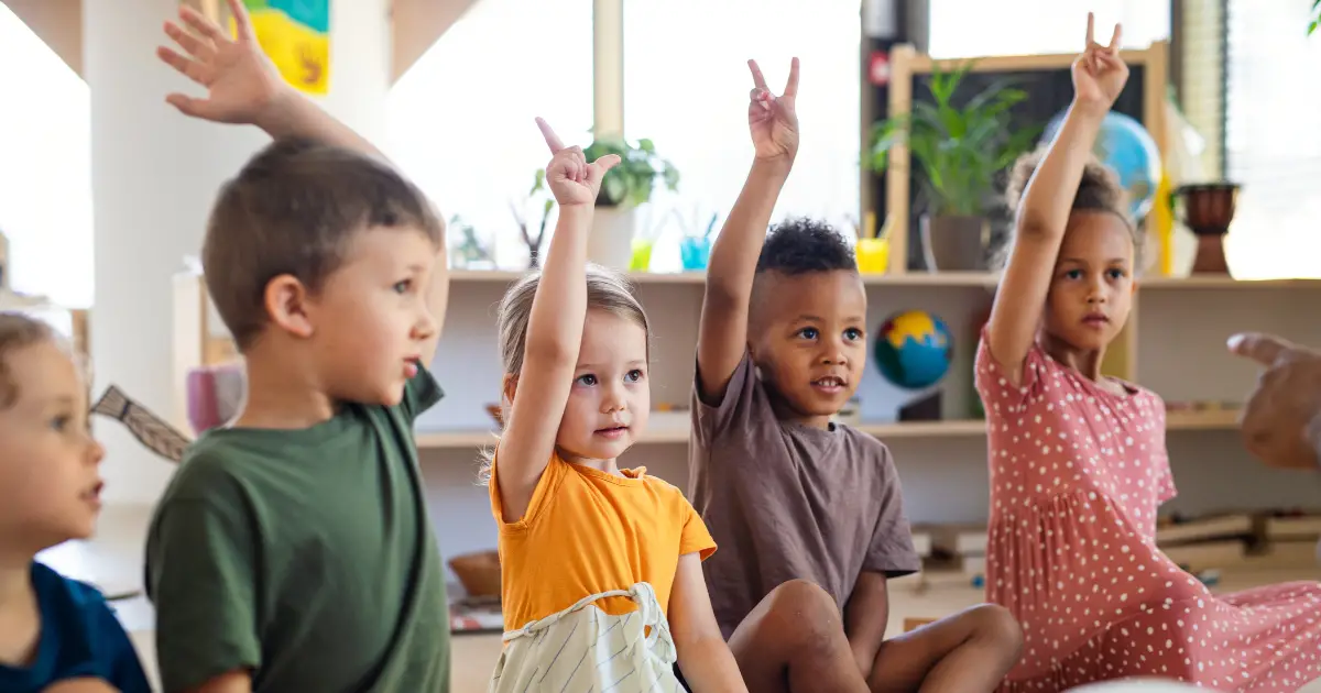 A class of kindergarten students raising their hands.